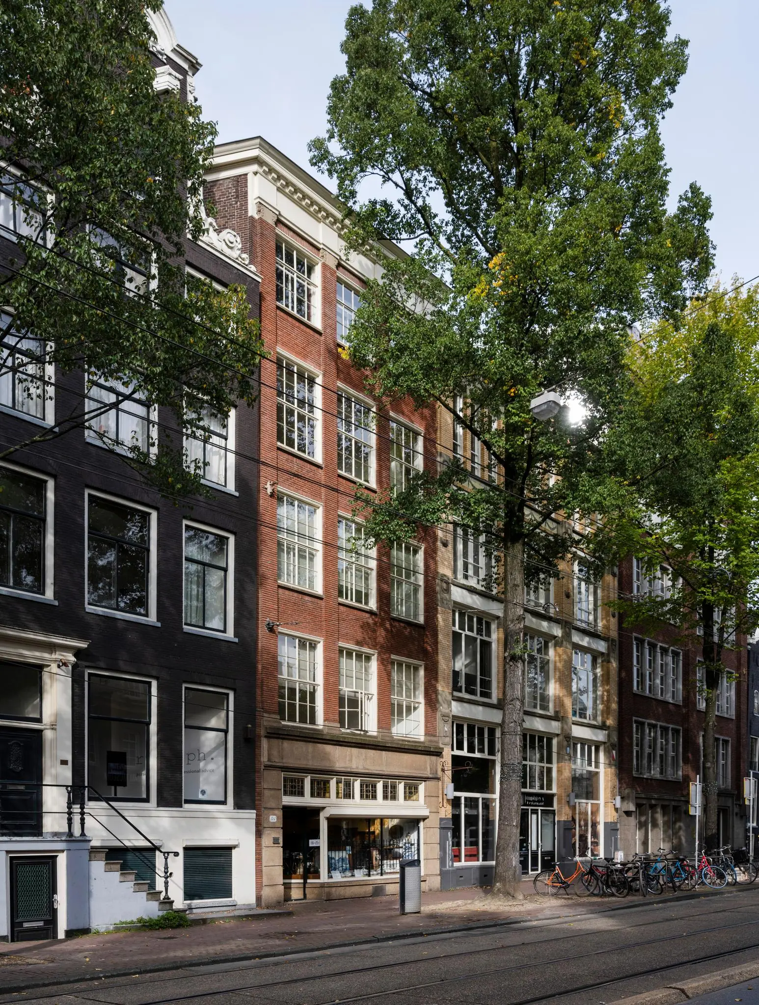 Gevels van historische panden aan de Nieuwezijds Voorburgwal in Amsterdam met fietsen en tramrails op de voorgrond.